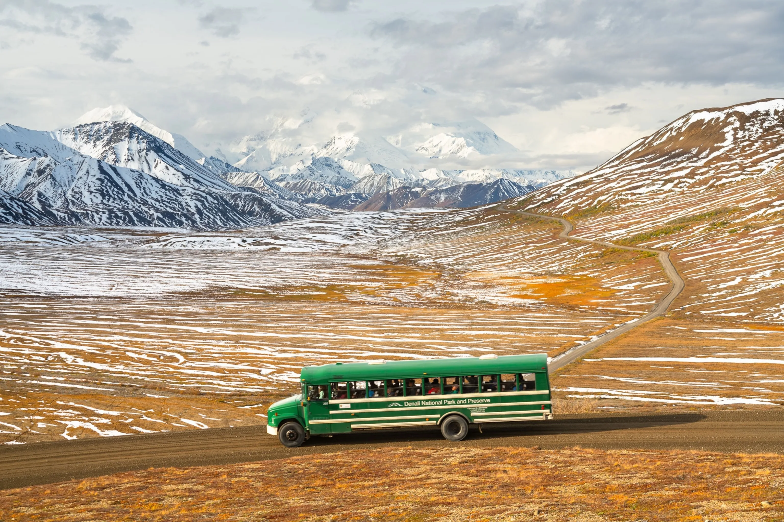 Green transit bus carrying visitors through Denali National Park, a key experience near Alaska cities.
