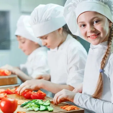 Group of children learning to prepare vegetables in a kitchen setting during a cooking camp
