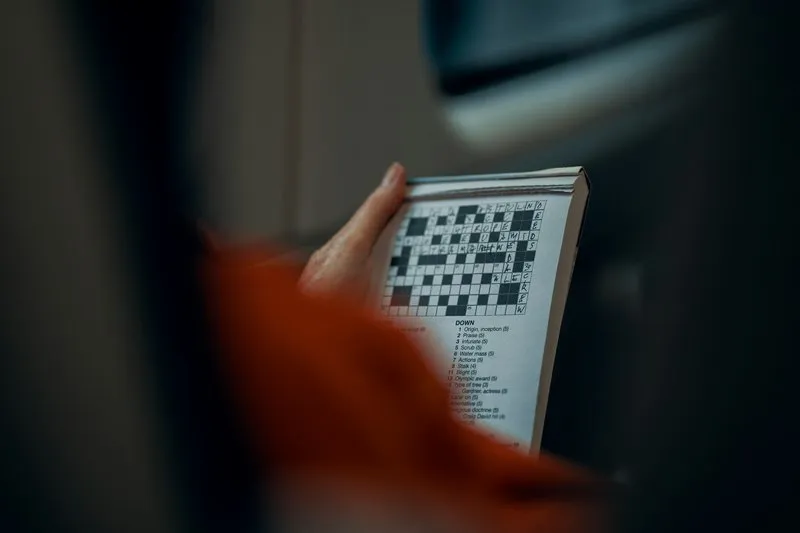 Hands solving a crossword puzzle, a popular pastime originating in New York City