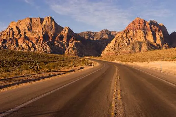 Highway driving through Red Rock Canyon National Conservation Area with towering red cliffs