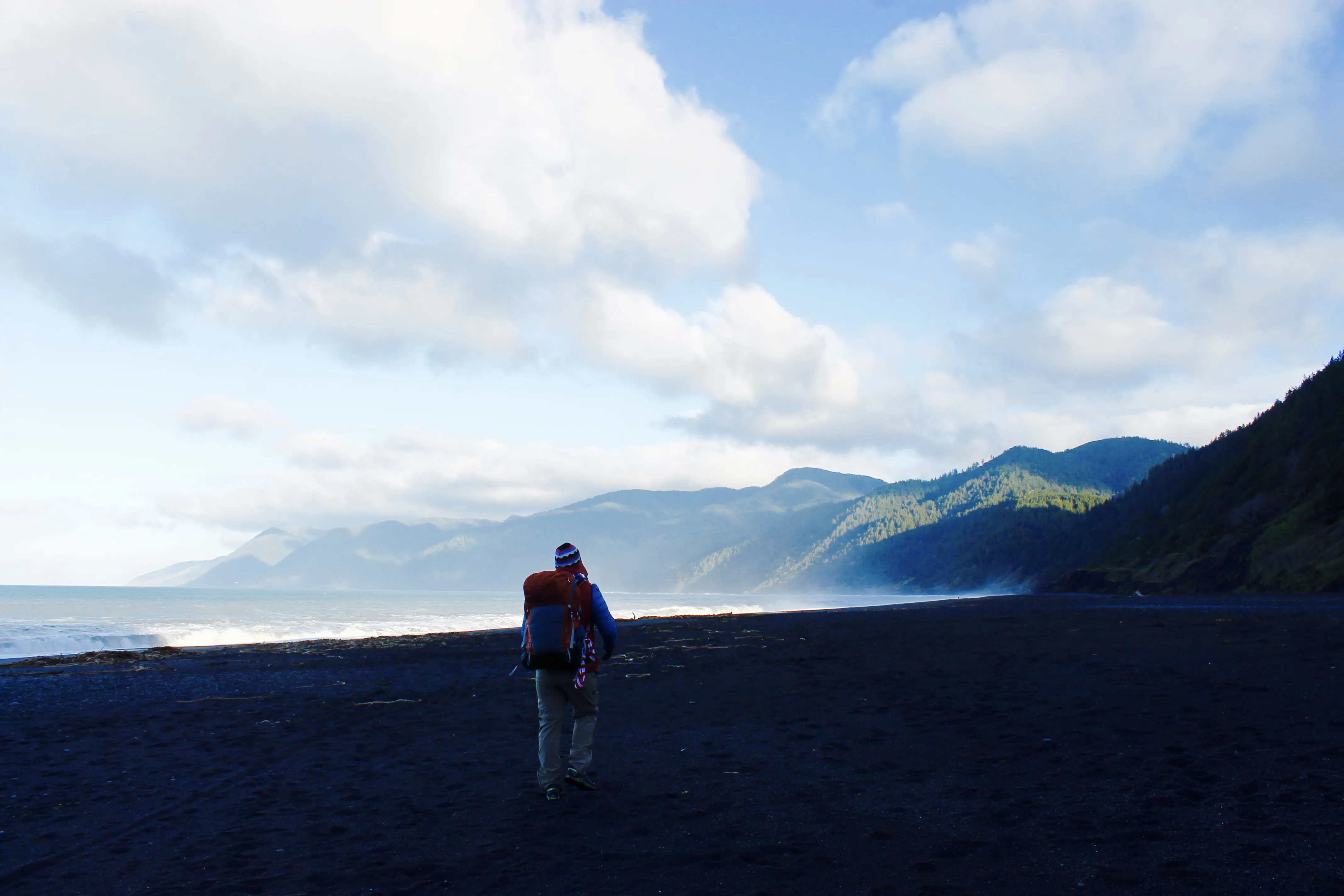 Hiker standing on a coastal trail overlooking the ocean and mountains