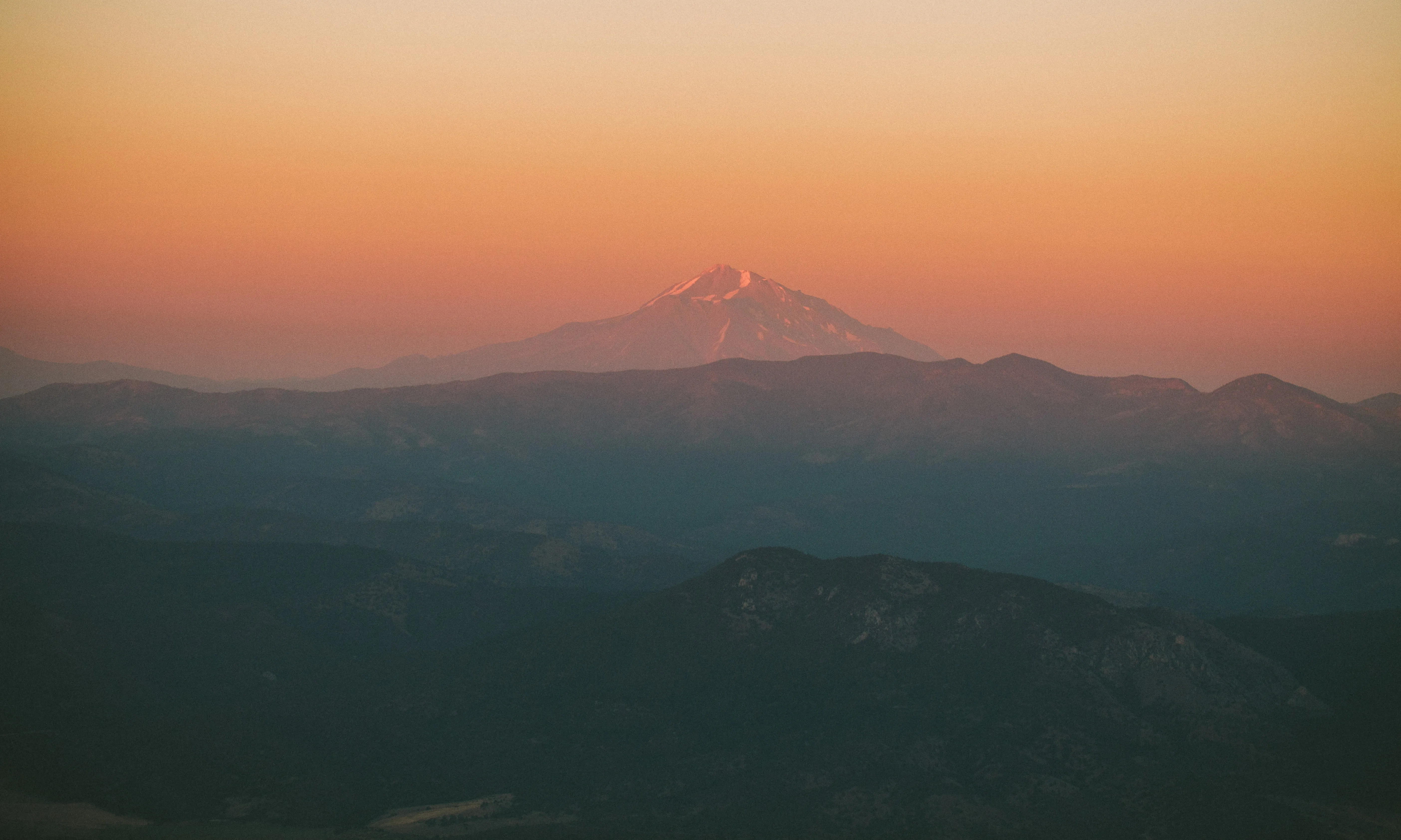 Hiker standing on a rocky summit overlooking distant mountains including Mt Shasta