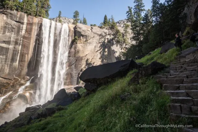 Hikers ascend wet stone steps on the Mist Trail alongside a powerful waterfall in Yosemite
