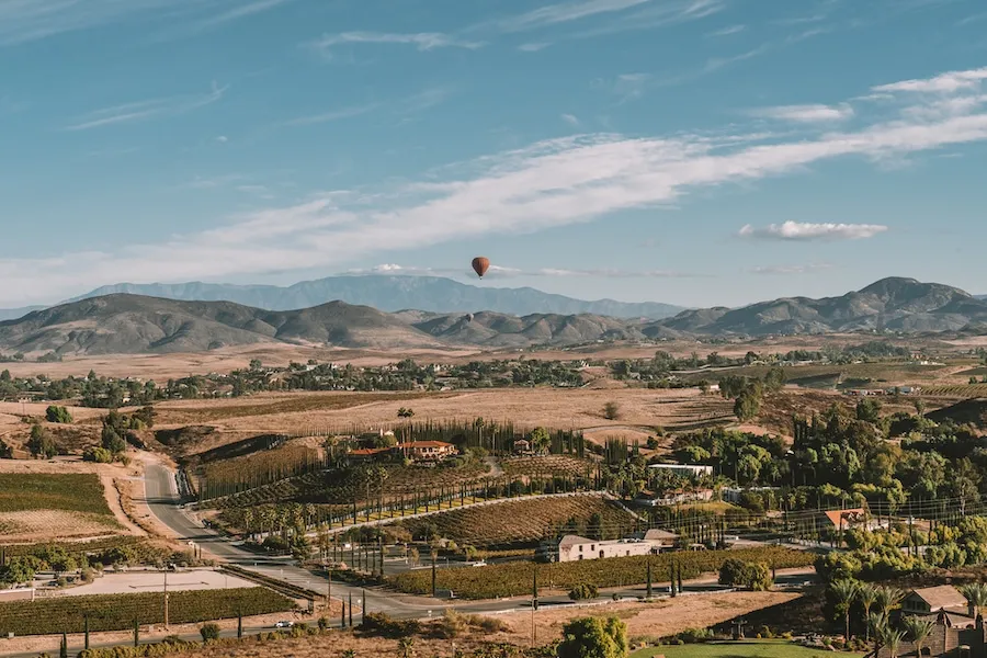 Hot air balloon floating over vineyards and hills in Temecula at sunrise