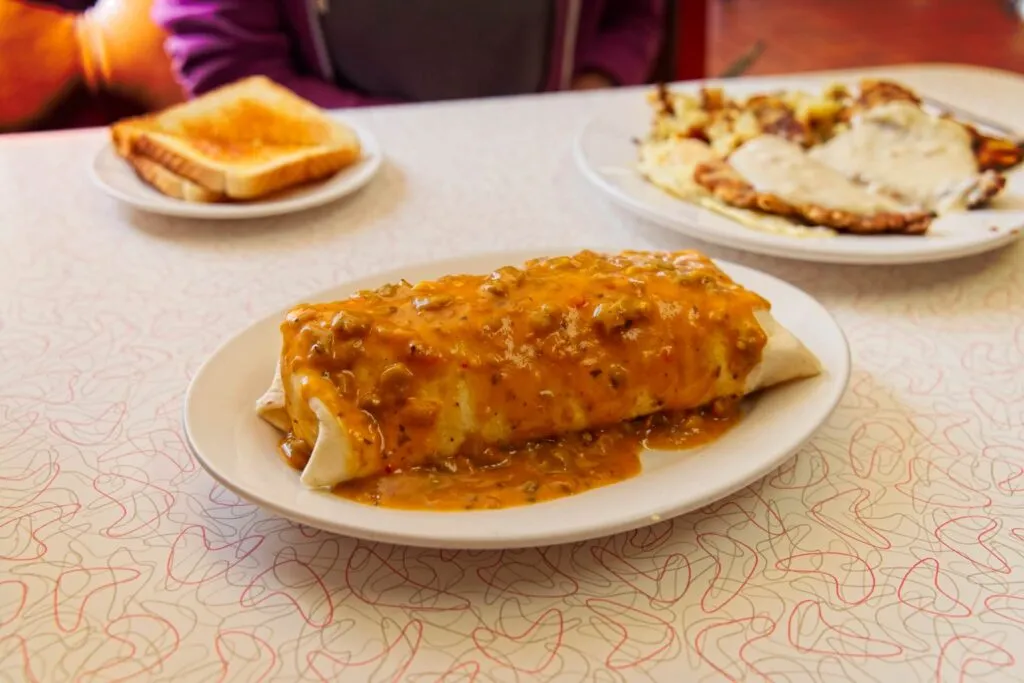 Huge smothered breakfast burrito with green chile, eggs, bacon, and cheese at Butcher Block Cafe, a classic cheap brunch spot in Denver.
