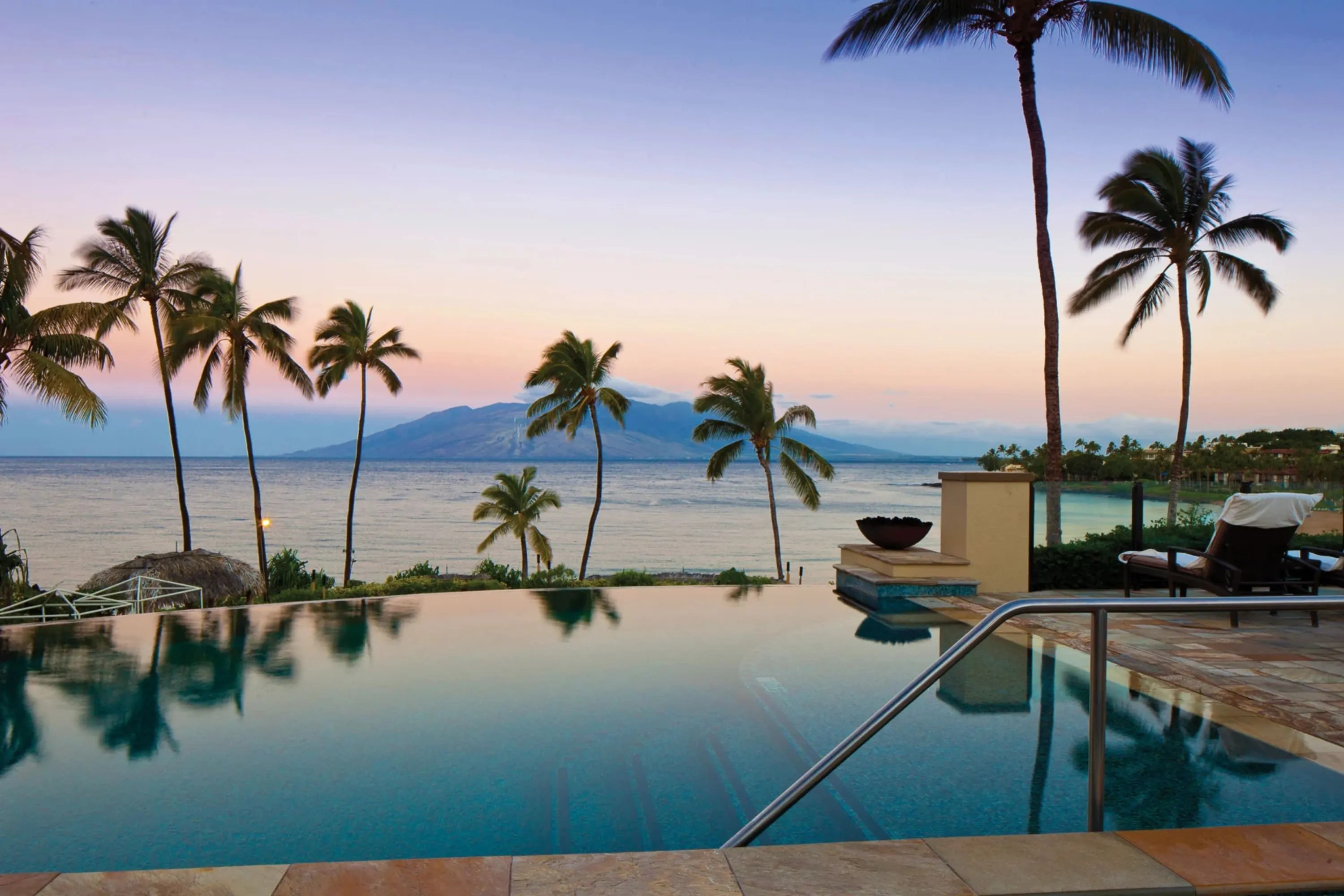 In the foreground: a sapphire-water infinity pool and attached balcony overlooks the ocean, with a mountain in the distance across a large body of water