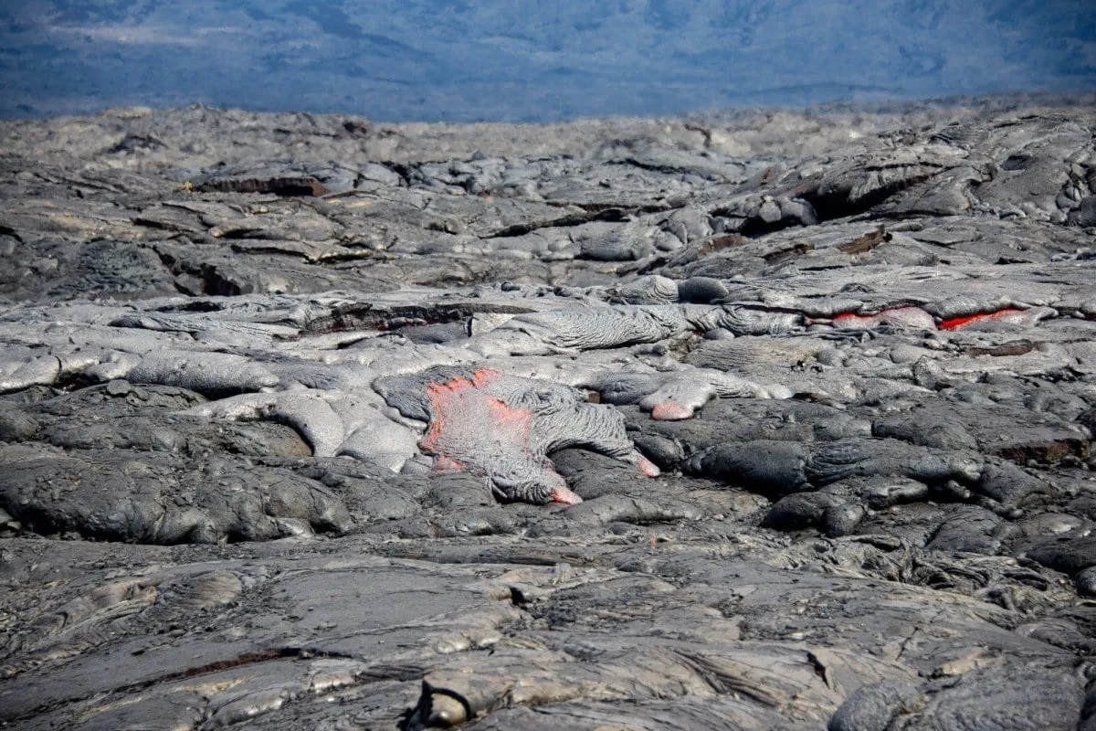 Lava flowing from a volcano across a rugged landscape in Hawaii Volcanoes National Park.
