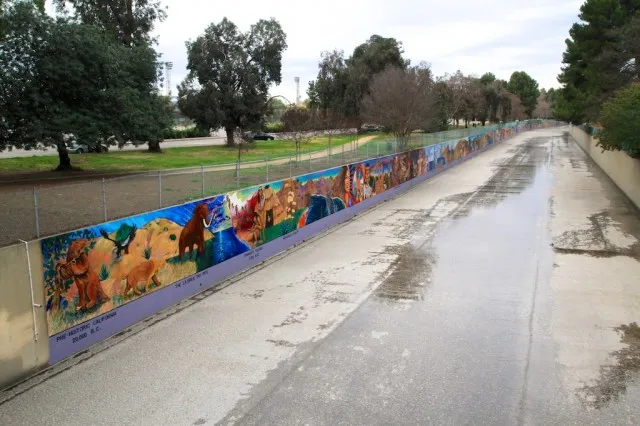 Long outdoor mural painted on a wall depicting historical scenes