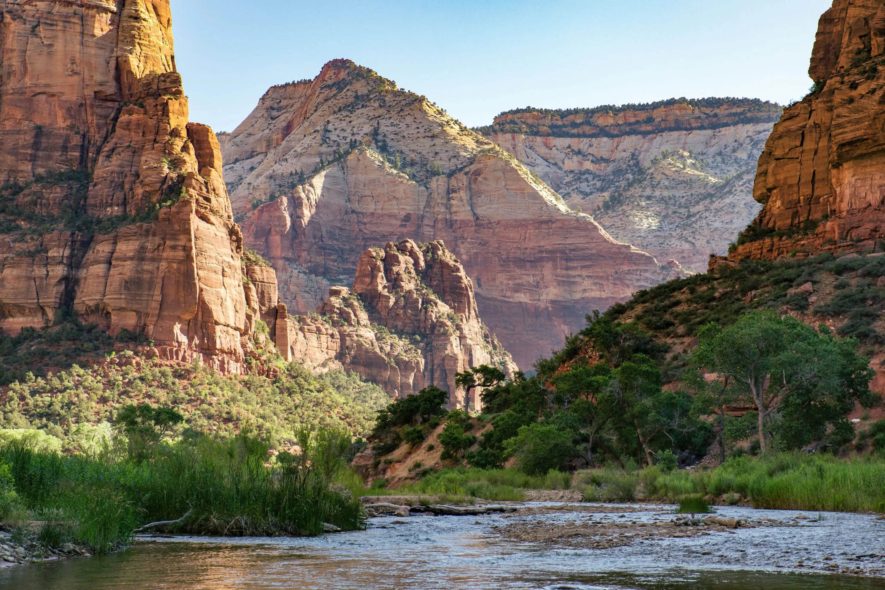 Lush vegetation surrounds a small, flowing stream with colorful mountains rising up