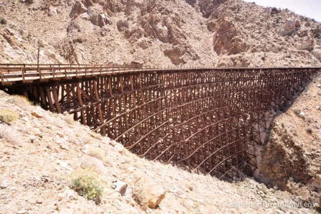 Massive wooden railroad trestle spanning a deep canyon in a desert landscape
