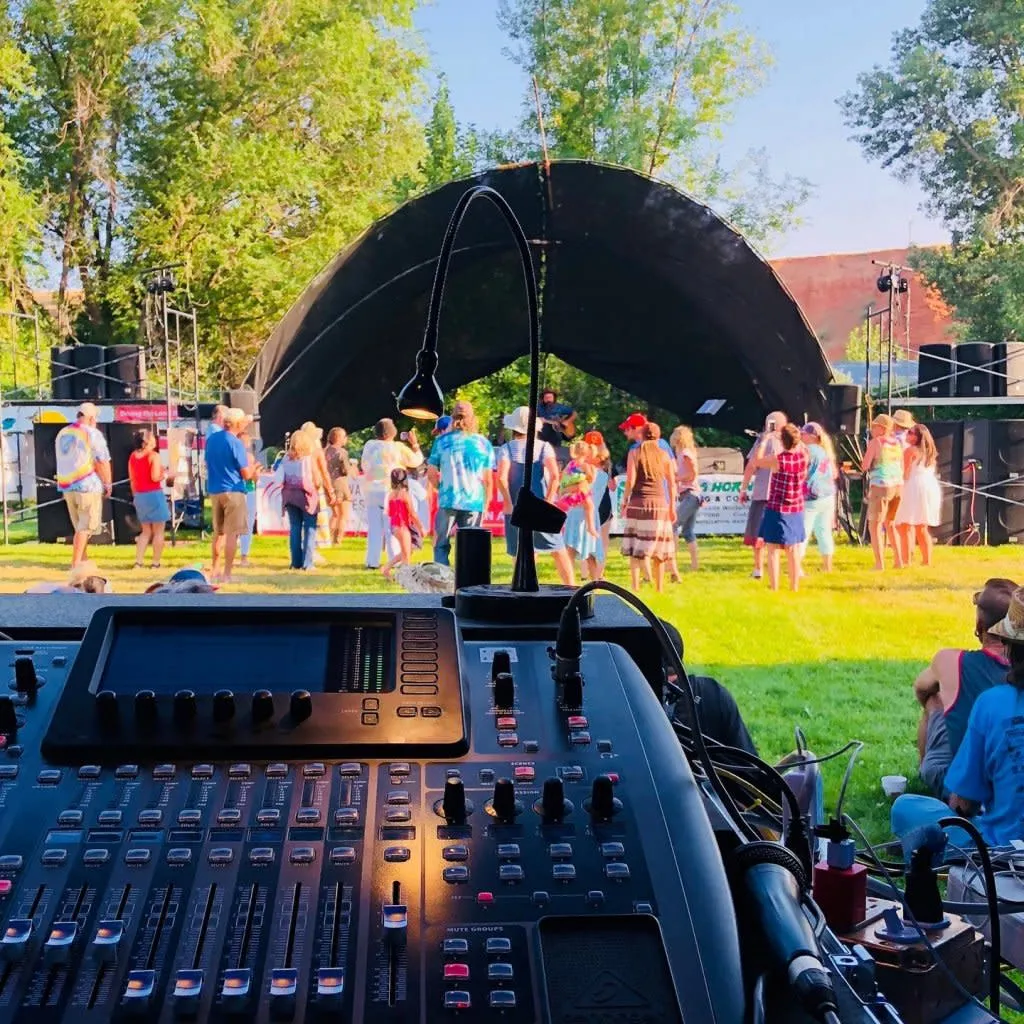 Musicians performing on stage at the Nowoodstock Music Festival in Ten Sleep, Wyoming with mountains in background