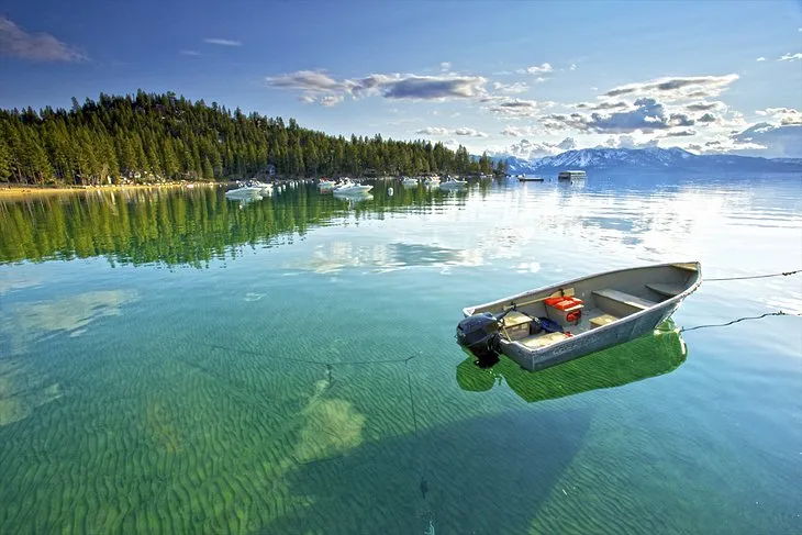Panoramic view of the clear blue water of Lake Tahoe surrounded by mountains and trees, a popular day trip from Reno.