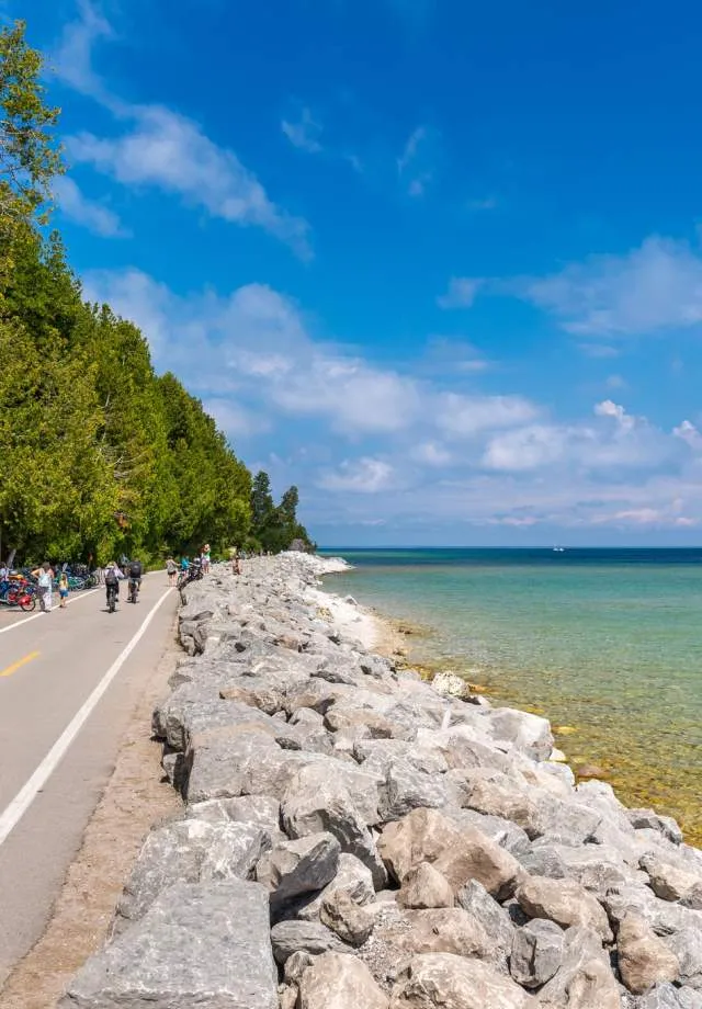 People biking on a paved path on Mackinac Island, surrounded by trees