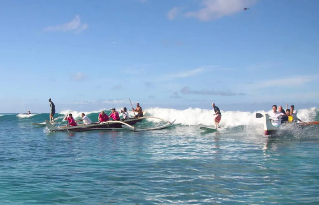 People surfing a wave in a traditional Hawaiian outrigger canoe off Waikiki Beach