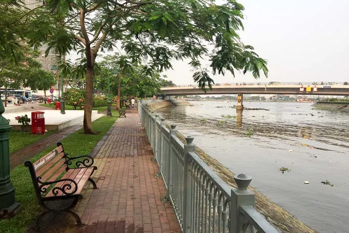 People walking along a paved pedestrian path beside the Saigon River