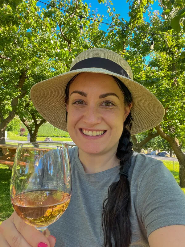 Person holding a glass of white wine with a vineyard in the background in Yakima