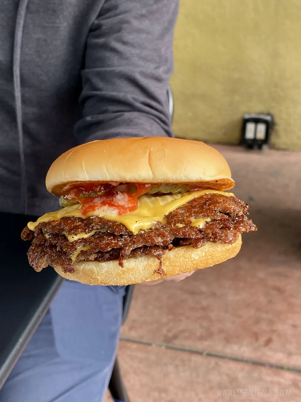 person holding a triple stack cheeseburger from Burgers Never Say Die, a recommended eat on a Los Angeles itinerary