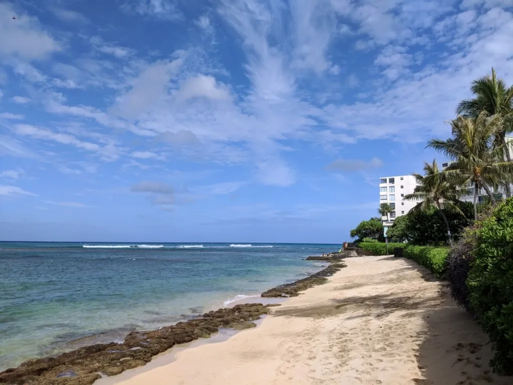 Quiet shoreline of Mākālei Beach Park with narrow sand and palm trees, offering a secluded experience near the Best Beach In Honolulu