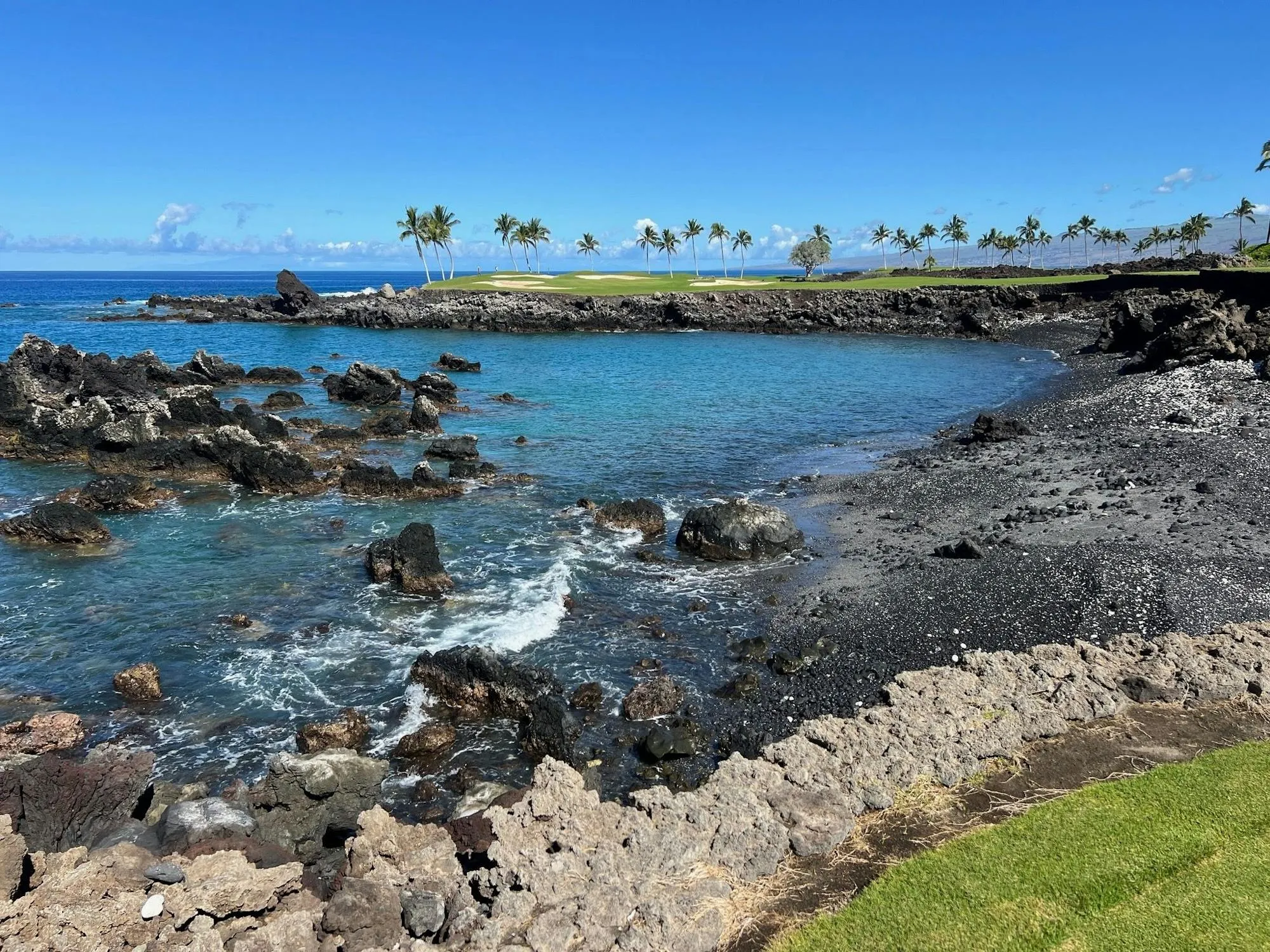 Rocky black-sand beach with a gold course in the distance