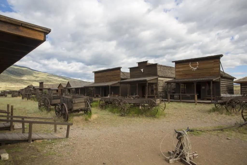 Row of historic wooden buildings and wagons at Old Trail Town in Cody - Western Things To See And Do In Wyoming