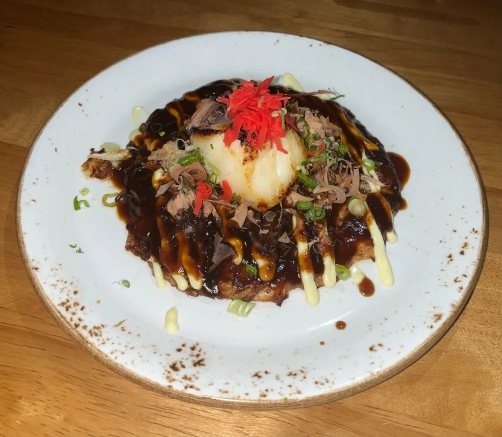 Savory BBQ Chilean Sea Bass Okonomiyaki topped with sauce and bonito flakes