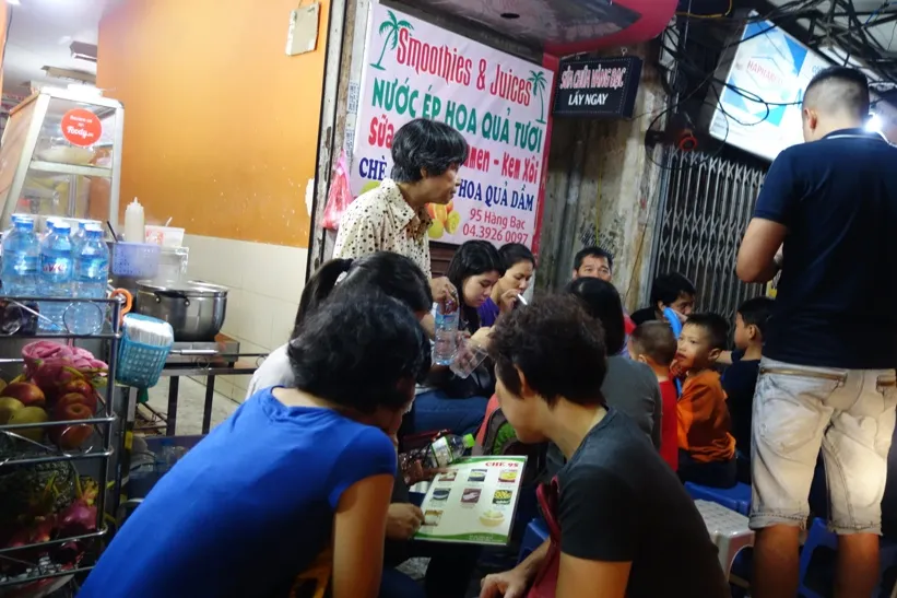 Small plastic stools and low tables crowded near the entrance of a dessert stall in Hanoi
