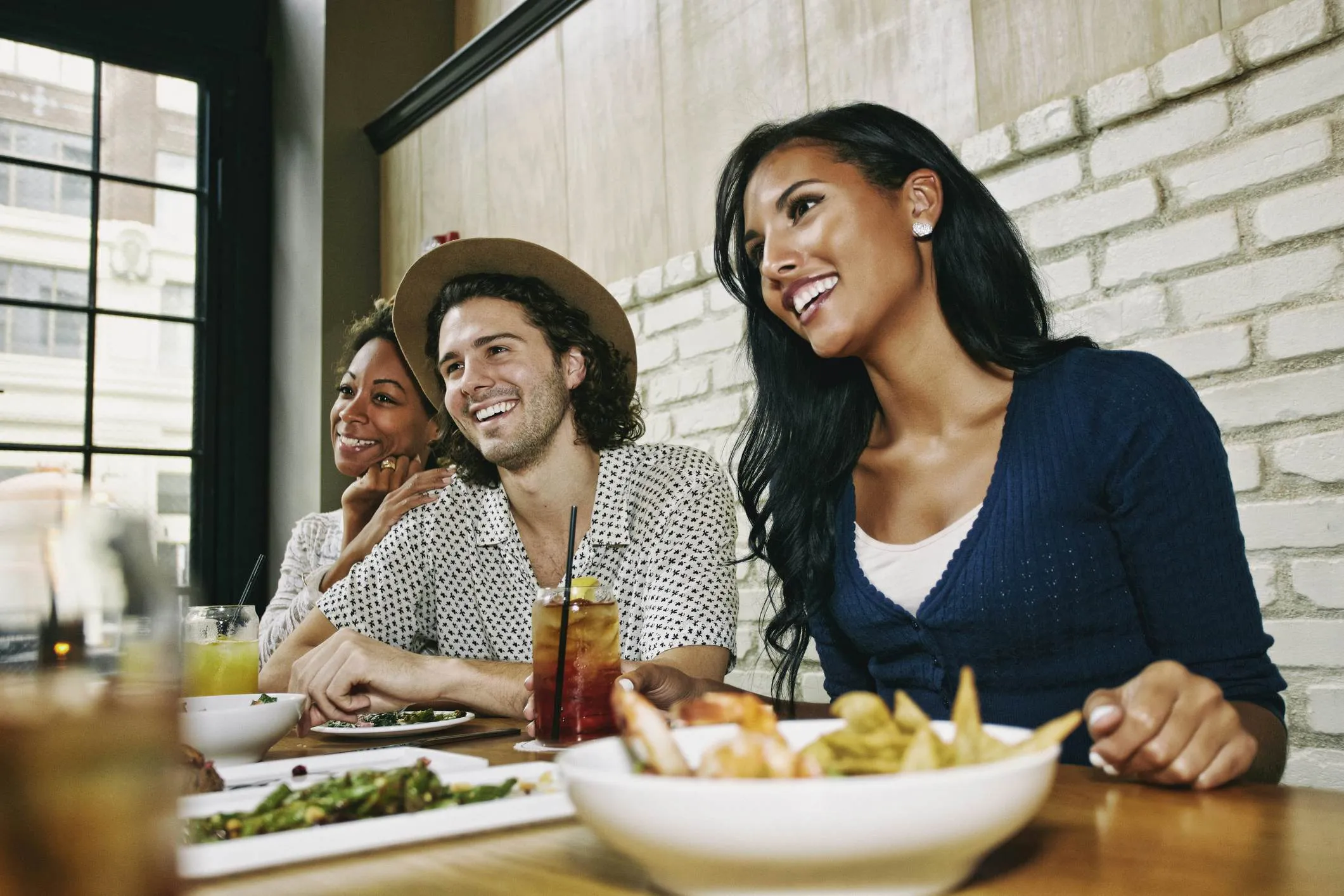Smiling friends enjoying food and cocktails at table in bar