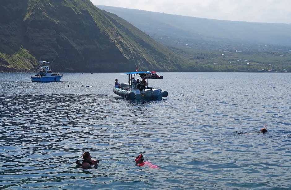 Snorkelers in the water at Captain Cook Monument, with smaller tour boats in the background.
