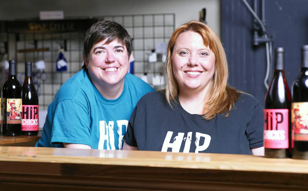 Staff members smiling behind the tasting bar at Hip Chicks Do Wine urban winery in Portland.