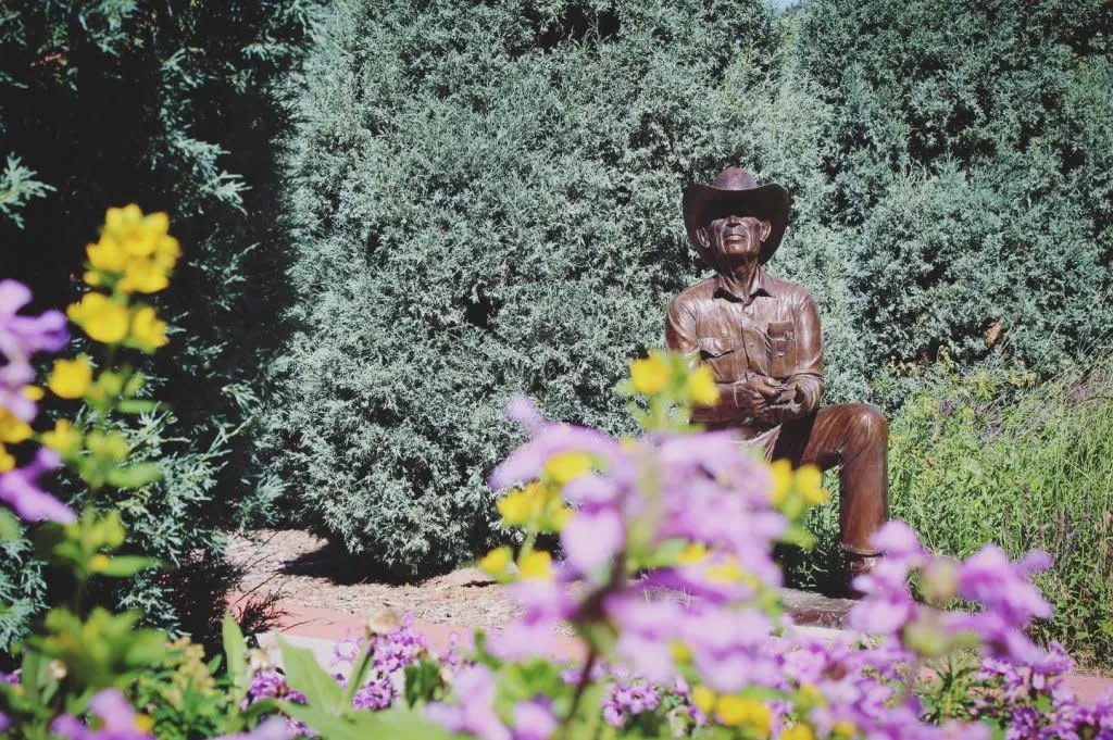 Statue beside a garden wall and purple flowers at the Cheyenne Botanic Gardens - Things To See And Do In Wyoming