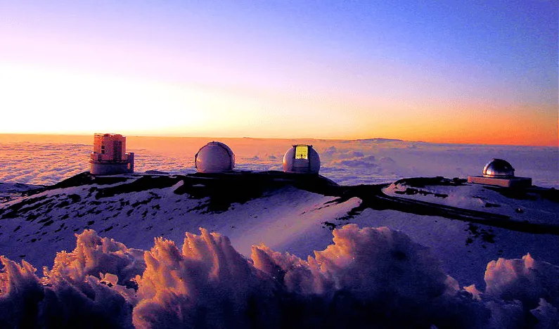 Sunrise view from the summit of Mount Haleakala in Maui, with clouds and observatories.
