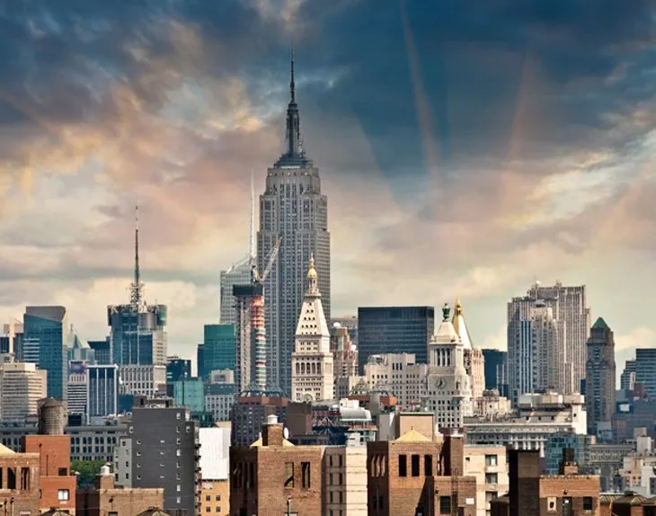 The art deco spire of the Empire State Building against a blue sky in New York.