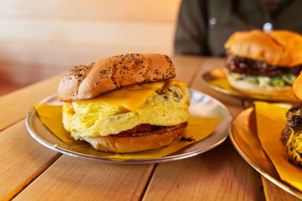 &quot;The Basic&quot; breakfast sandwich with egg, bacon, and hash brown on a kaiser roll at Odie B's (formerly Bodega), known for great sandwiches and brunch in Denver.