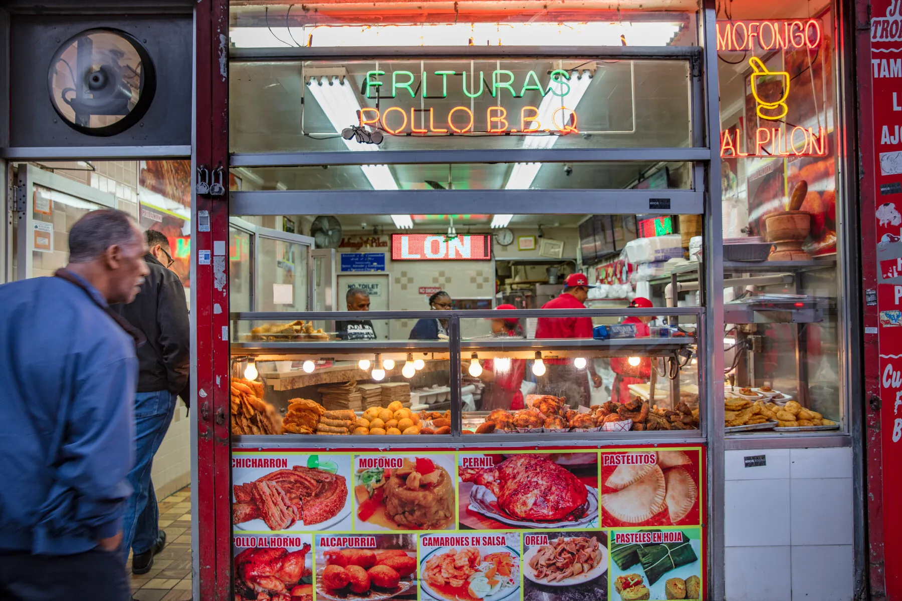 The colorful neon sign and window display of fried foods at 188 Bakery Cuchifritos.