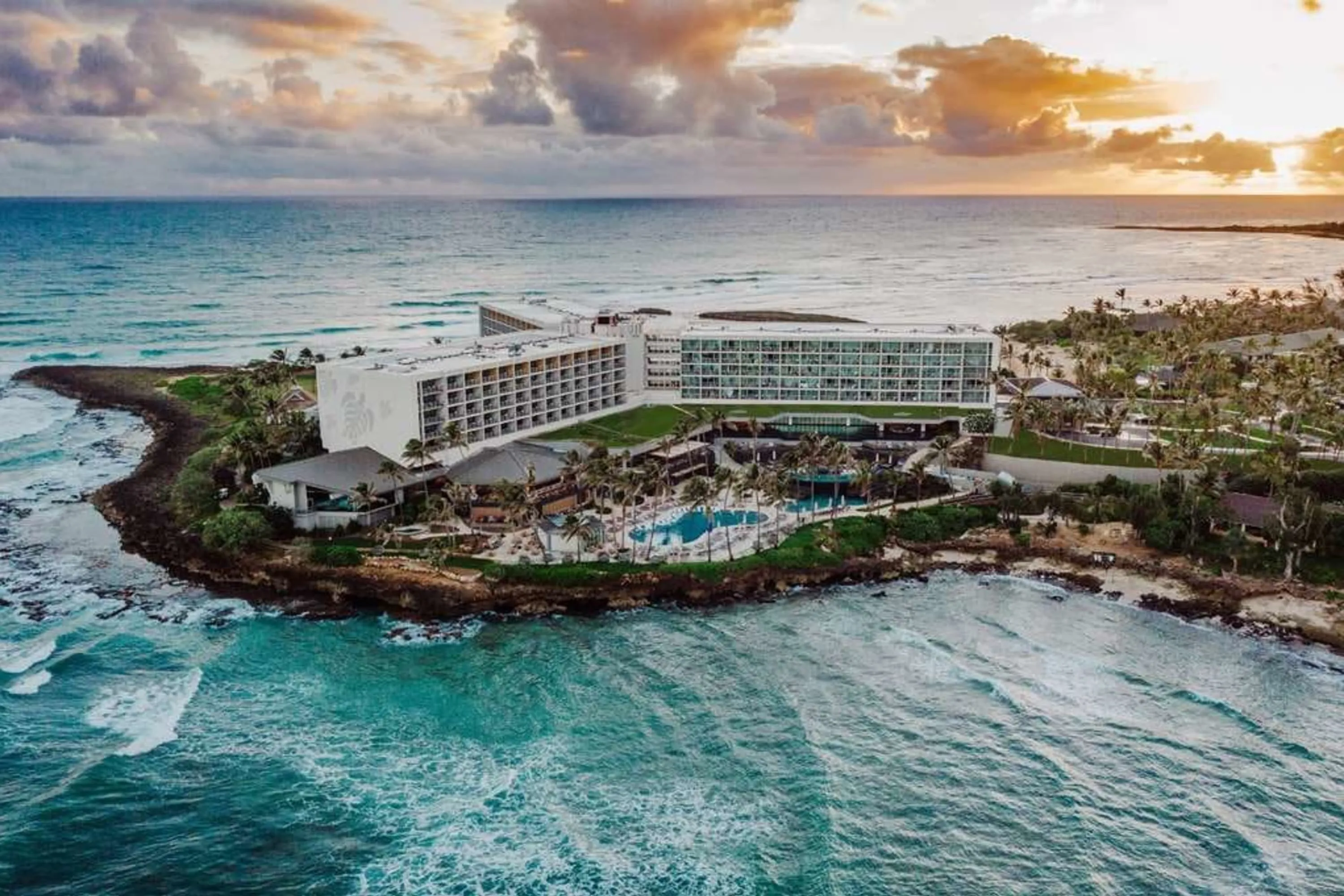 The grounds of The Ritz-Carlton O‘ahu, Turtle Bay alone on a small peninsula surrounded by beautiful water and under cloudy skies as the sun sets