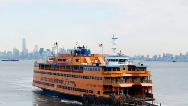 The iconic orange Staten Island Ferry crosses the harbor with the New York City skyline in the background