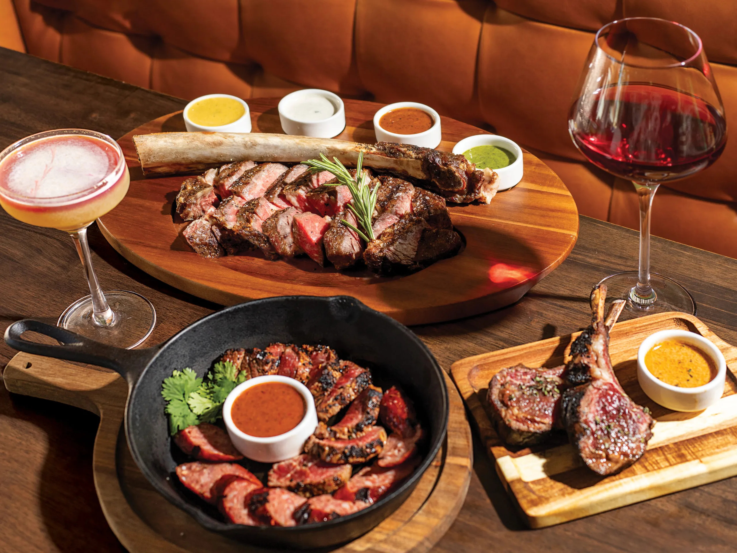 Three distinct meat dishes presented on a dark, rustic wood table: steak slices, duck confit, and tri-tip