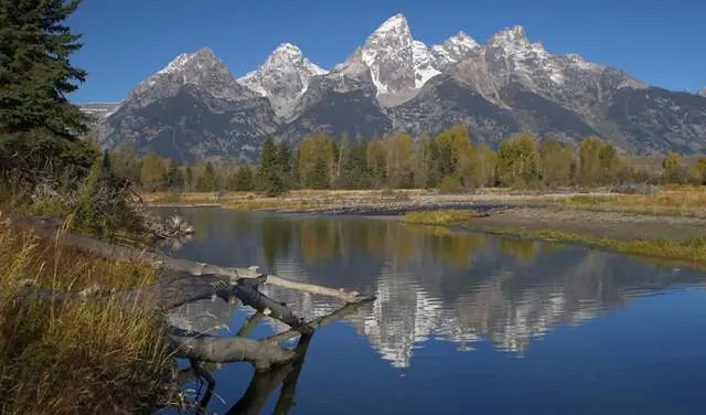 Three hikers on a trail with Grand Teton mountain range in the background.