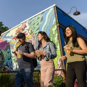 Three people walk past a vibrant street mural in the Alberta Arts District, ready for a walking tour in Portland Oregon.