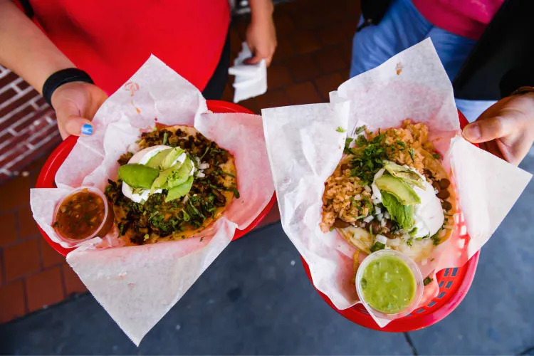 Two people holding small red baskets with tacos in them, perfect for a Las Vegas food tour date idea
