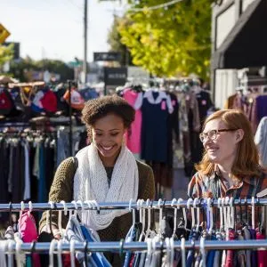 two people look through outdoor racks of vintage clothing on a sunny day, highlighting shopping opportunities in Portland Oregon