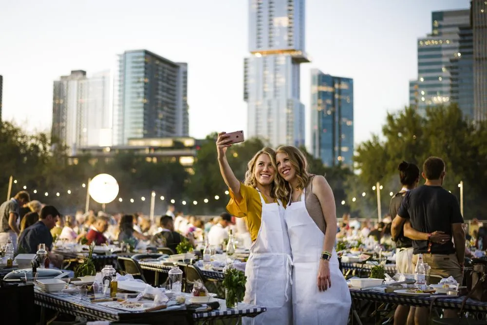 Two women smiling take a selfie with the Austin skyline behind them at the austin food and wine festival