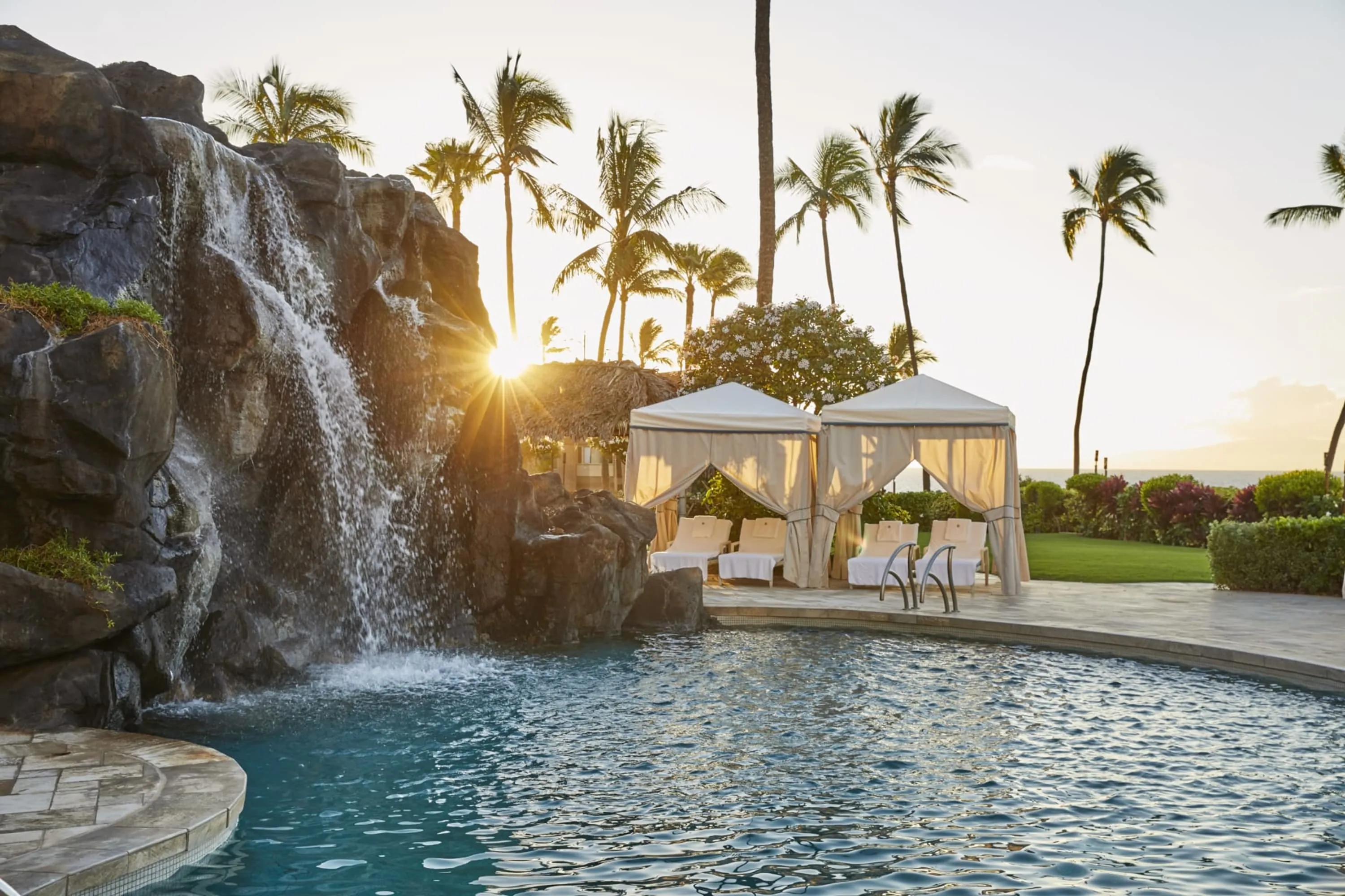 Water pours down rocks into a large pool flanked by tented loungers