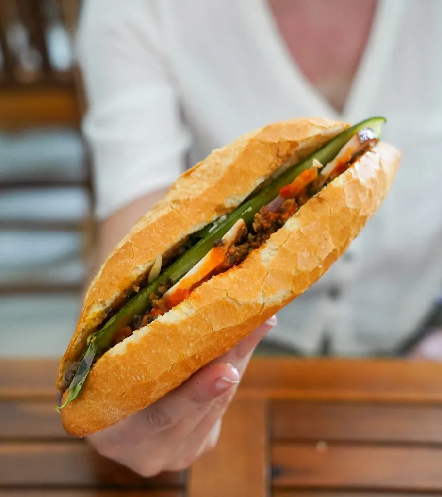 Woman adding ingredients to a banh mi behind a counter