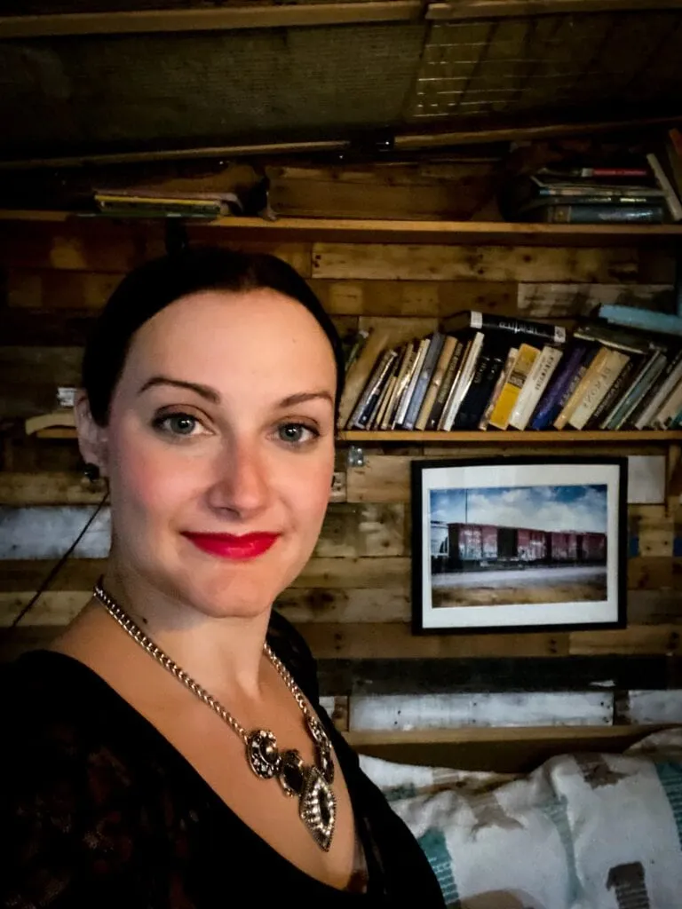 Woman posing in front of bookshelves, representing exploring unique cultural events like the Edgar Allan Poe Ball in Austin.