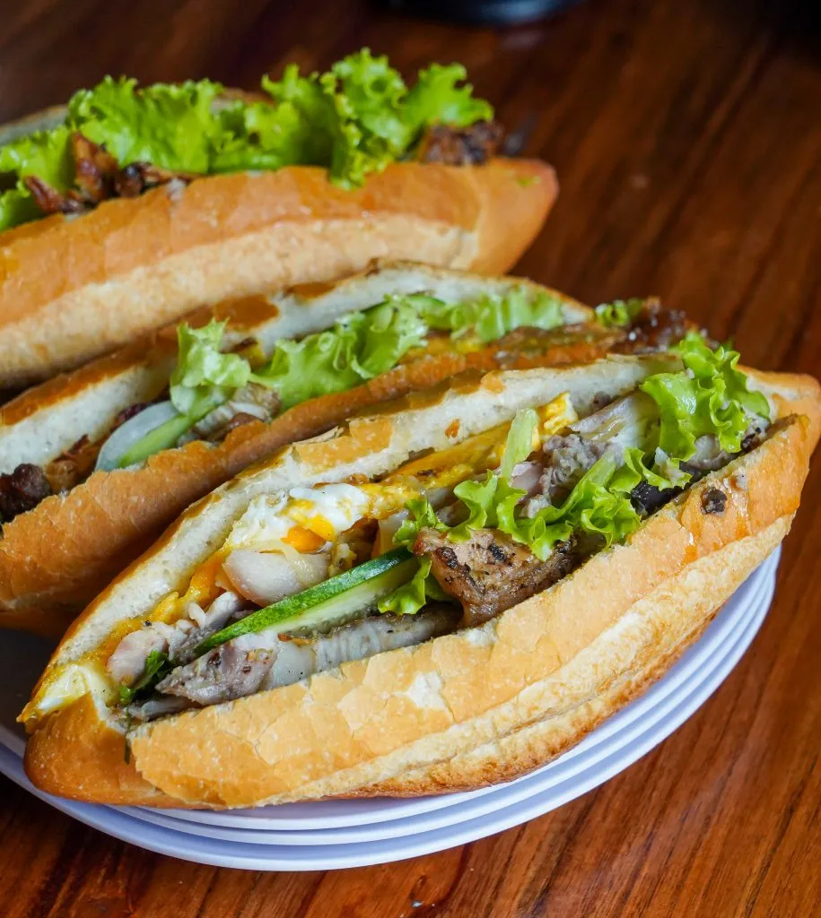 Woman preparing banh mi sandwiches at a busy street stall