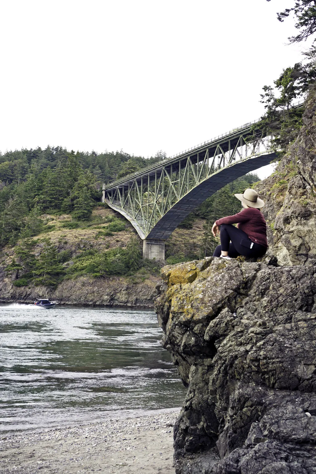 Woman sitting on a rock with the Deception Pass Bridge in the background