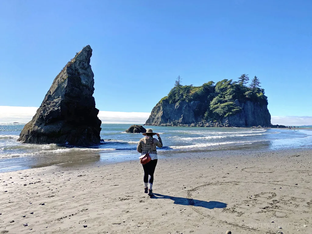 Woman walking along a misty, driftwood-strewn beach on the Washington coast