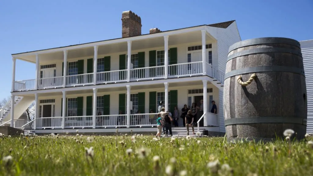 Wooden barrel in the foreground and people on the steps of the Old Bedlam building at Fort Laramie National Historic Site - Historic Things To See And Do In Wyoming